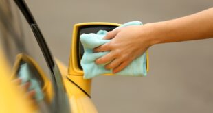 Une personne nettoie le rétroviseur extérieur d’une voiture avec un chiffon en microfibre.